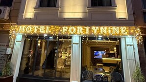 Une façade d’hôtel avec une enseigne lumineuse, un tapis rouge à l’entrée et un espace de réception bien visible, doté de sièges.