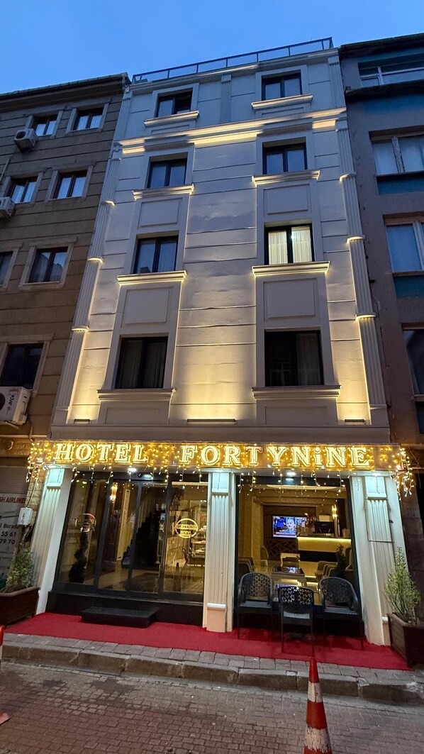 A hotel facade with illuminated signage, a red carpet entrance, and a visible reception area with seating. - FORTYNINE HOTEL (Istanbul)