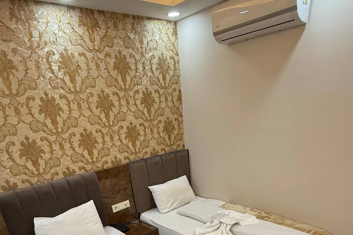 A hotel room with two beds, a patterned wallpaper, an air conditioning unit, and wooden flooring.