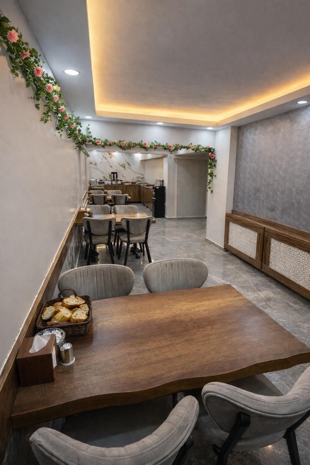 Un comedor con una mesa de madera, sillas tapizadas de color gris y una cocina al fondo.