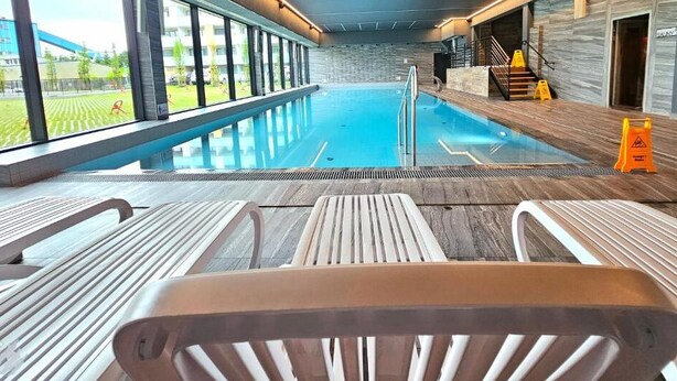 An indoor swimming pool with clear glass walls, wooden deck, and lounge chairs. - Apartament Glamour z basenem - 365PAM (Kolobrzeg)