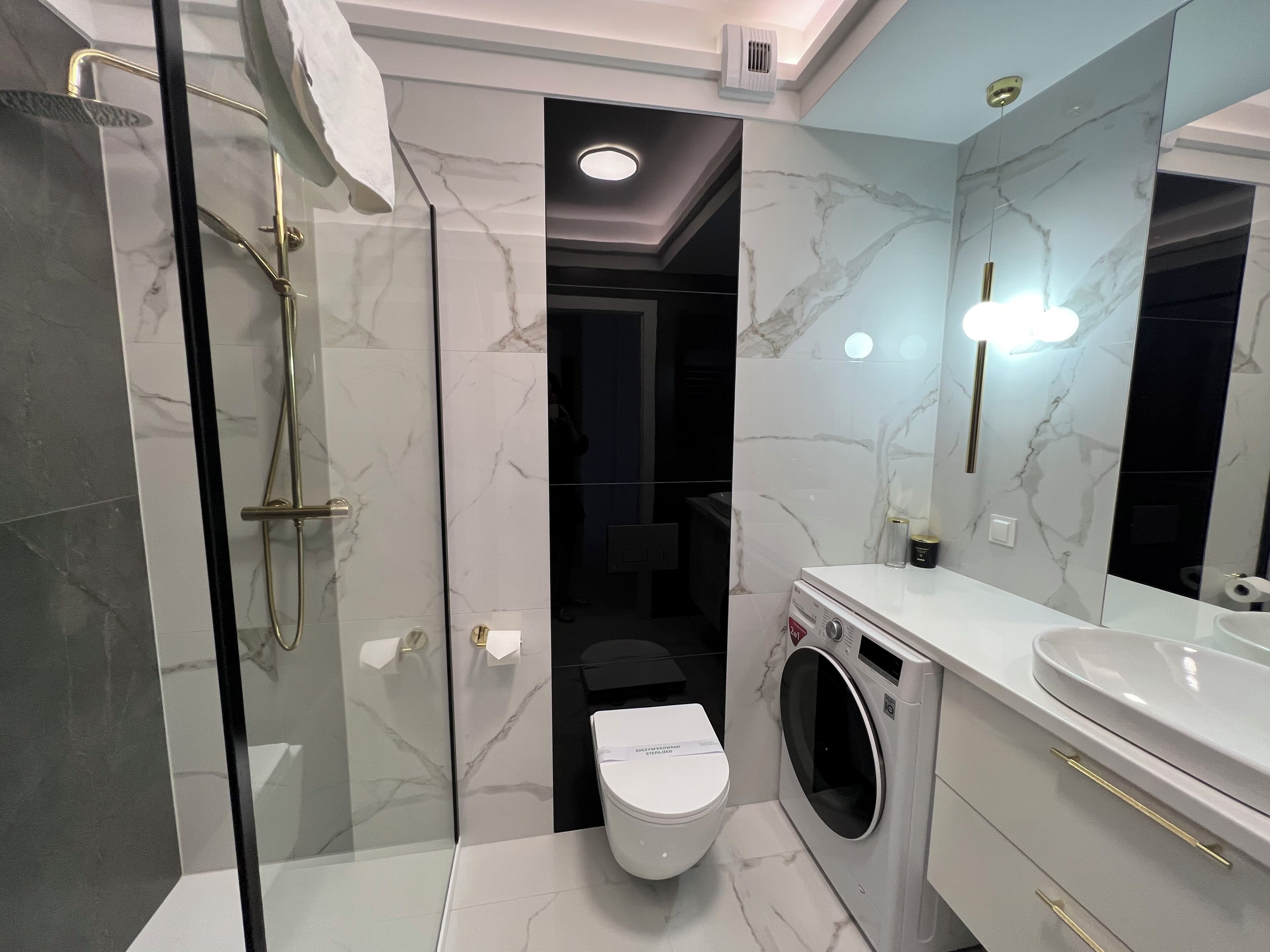 A modern bathroom with a glass-enclosed shower, a toilet, and a built-in washing machine.