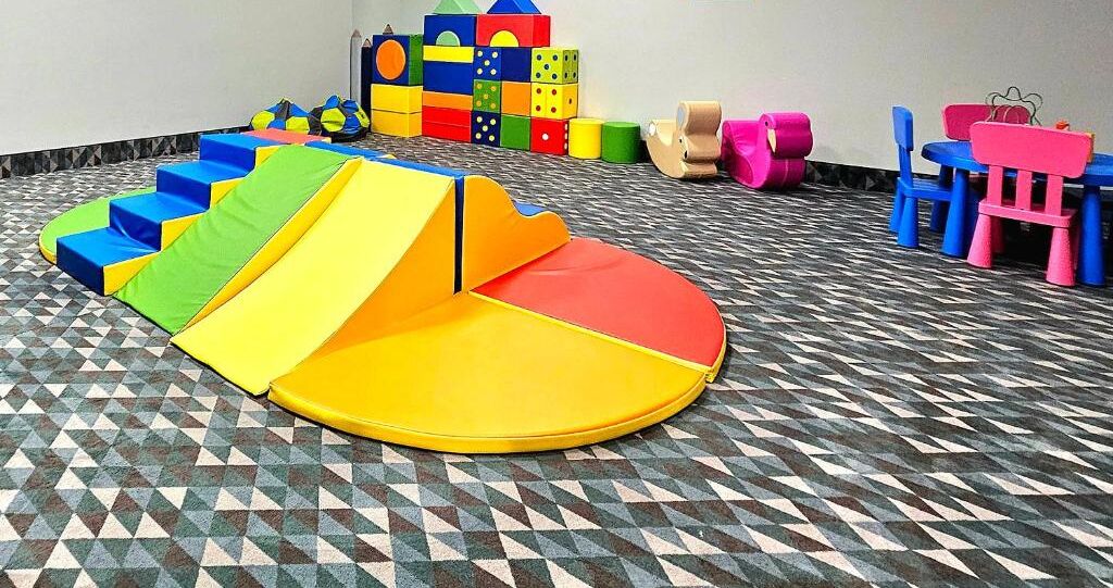A play area with a colorful slide, soft play mats, and a variety of toys and furniture.