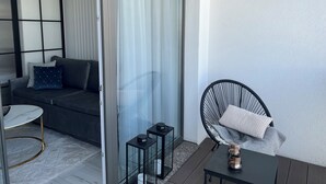 A modern living room with a sofa, a chair, a small table, and a glass door leading to an outdoor area. - Apartament Glamour z basenem - 365PAM (Kolobrzeg)