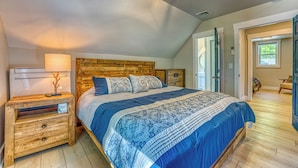 Un dormitorio con cabecera de madera, cama con ropa de cama azul, mesita de noche con lámpara y cómoda de madera.