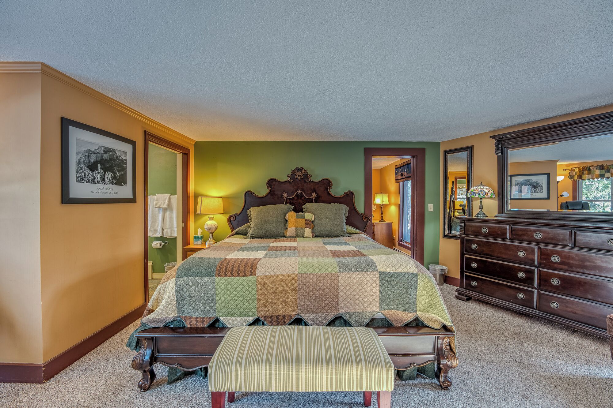 Quarto com uma cama grande, cômoda, banquinho e um quadro na parede.