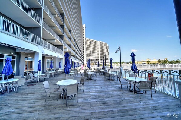 Terraza con mesas y sillas, sombrillas azules y vista a un edificio alto.