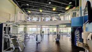 Un gimnasio con diverso equipamiento de ejercicios, un entrepiso y amplias ventanas con vistas.
