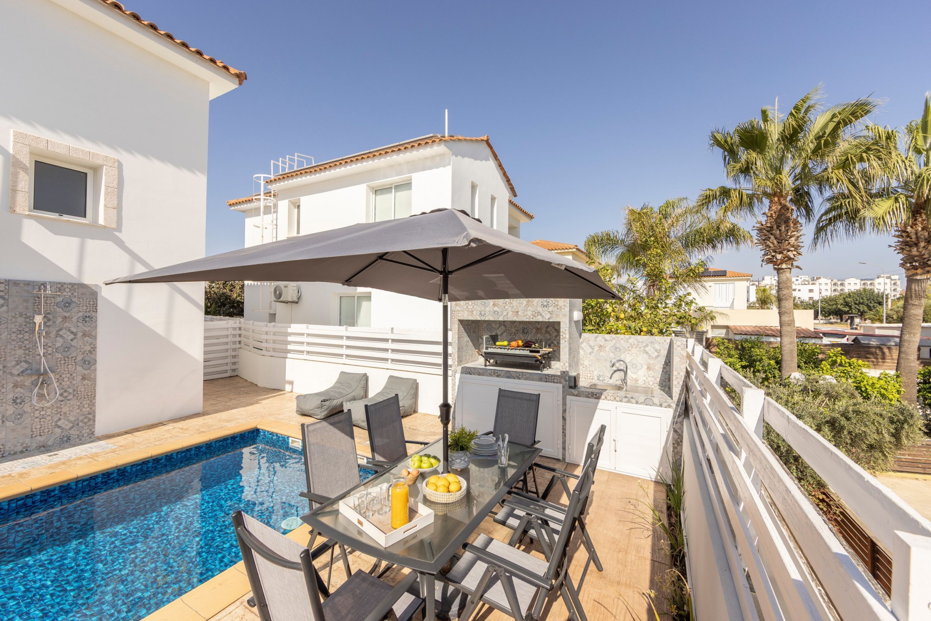 A poolside area with a dining table, chairs, and an umbrella.