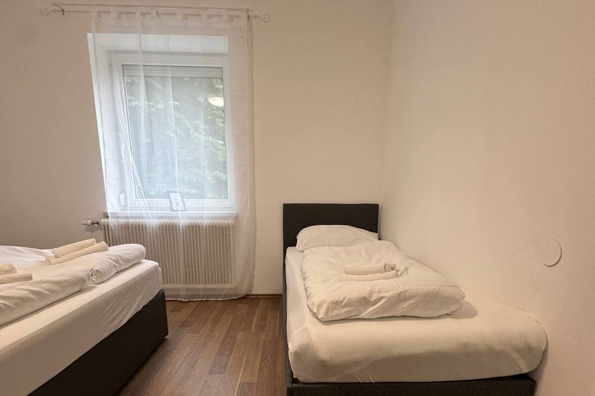 A room with two beds, a window with sheer curtains, and a radiator.