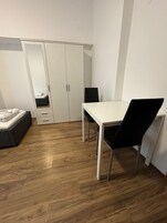 Una habitación pequeña y moderna con una cama, un armario blanco, una mesa de comedor con dos sillas y suelo de madera.