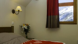A bedroom with a bed, a nightstand with a lamp, a vase of flowers, and a window with curtains. - 50m from ski slopes, balcony, tv, ski locker, 30m², Valloire (Valloire)