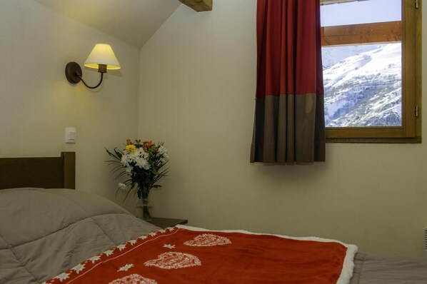 Ein Schlafzimmer mit einem Bett, einem Nachttisch mit Lampe, einer Blumenvase und einem Fenster mit Vorhängen.