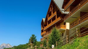 A multi-story wooden building with balconies, surrounded by greenery and a mountain in the background. - 50m from ski slopes, balcony, tv, ski locker, 30m², Valloire (Valloire)