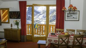 A dining area with a table set for four, a wooden cabinet, a framed picture, and a view of snow-covered mountains through a wooden door. - 50m from ski slopes, balcony, tv, ski locker, 30m², Valloire (Valloire)