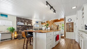 Een keuken met een centraal eiland, houten vloeren, witte kasten, een accentmuur van steen en een houten trap die naar een andere ruimte leidt.