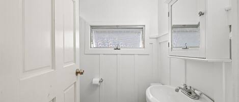 A small, white bathroom with a toilet, sink, and window.