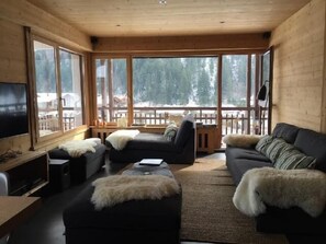 A cozy cabin interior with a large window offering a snowy mountain view, a black sofa, a small table, and a television on the left wall. - Wifi, 2nd floor, tv, 14m², Le Grand Bornand (Le Grand-Bornand)