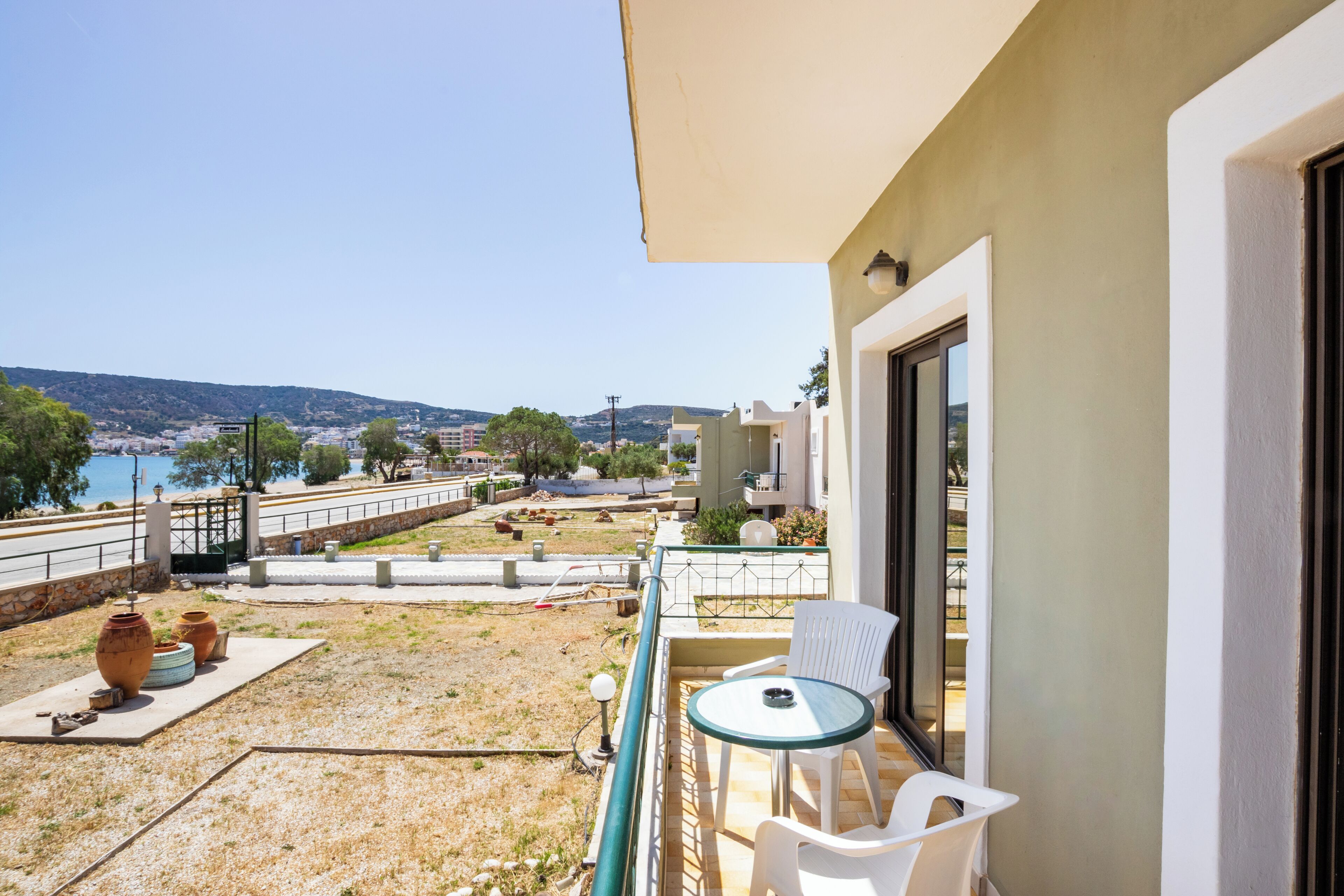 A balcony with a view of the sea, outdoor furniture, and a small garden area.
