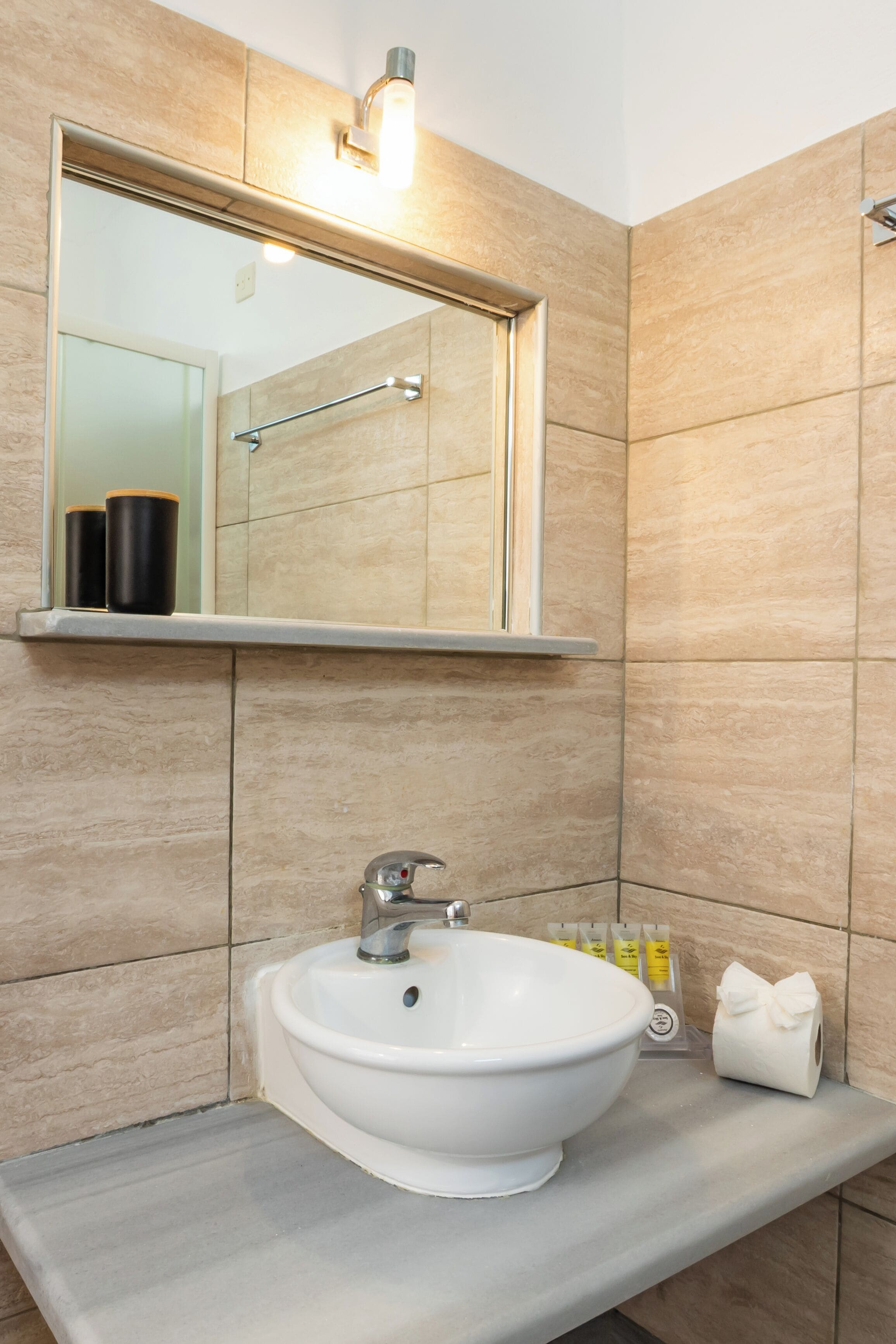A bathroom with a white sink, a mirror above it, and a towel dispenser.