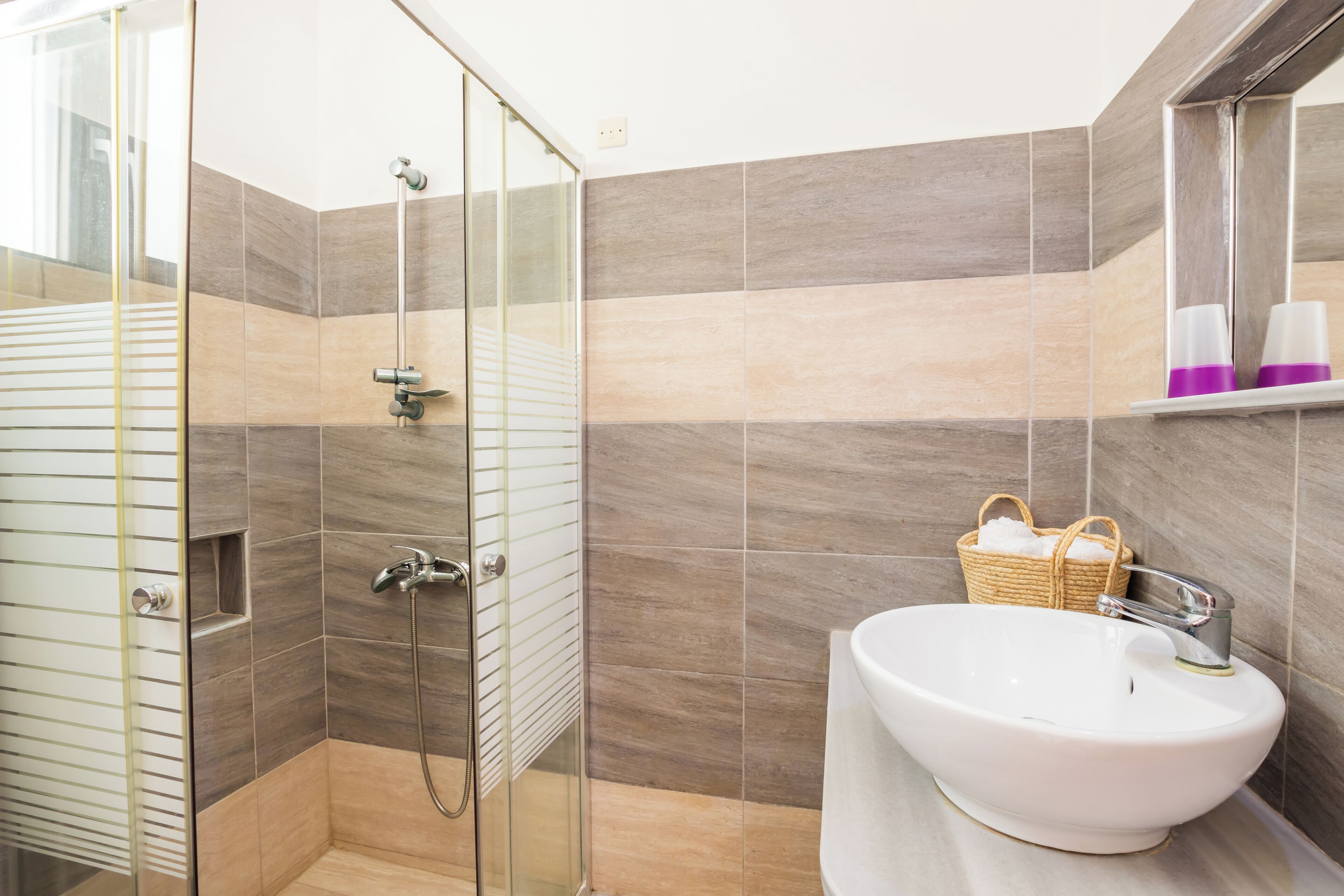 Un baño moderno con cabina de ducha de vidrio, un lavabo blanco y una cesta de mimbre en la pared.