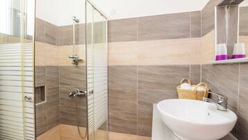 Un baño moderno con cabina de ducha de vidrio, un lavabo blanco y una cesta de mimbre en la pared.
