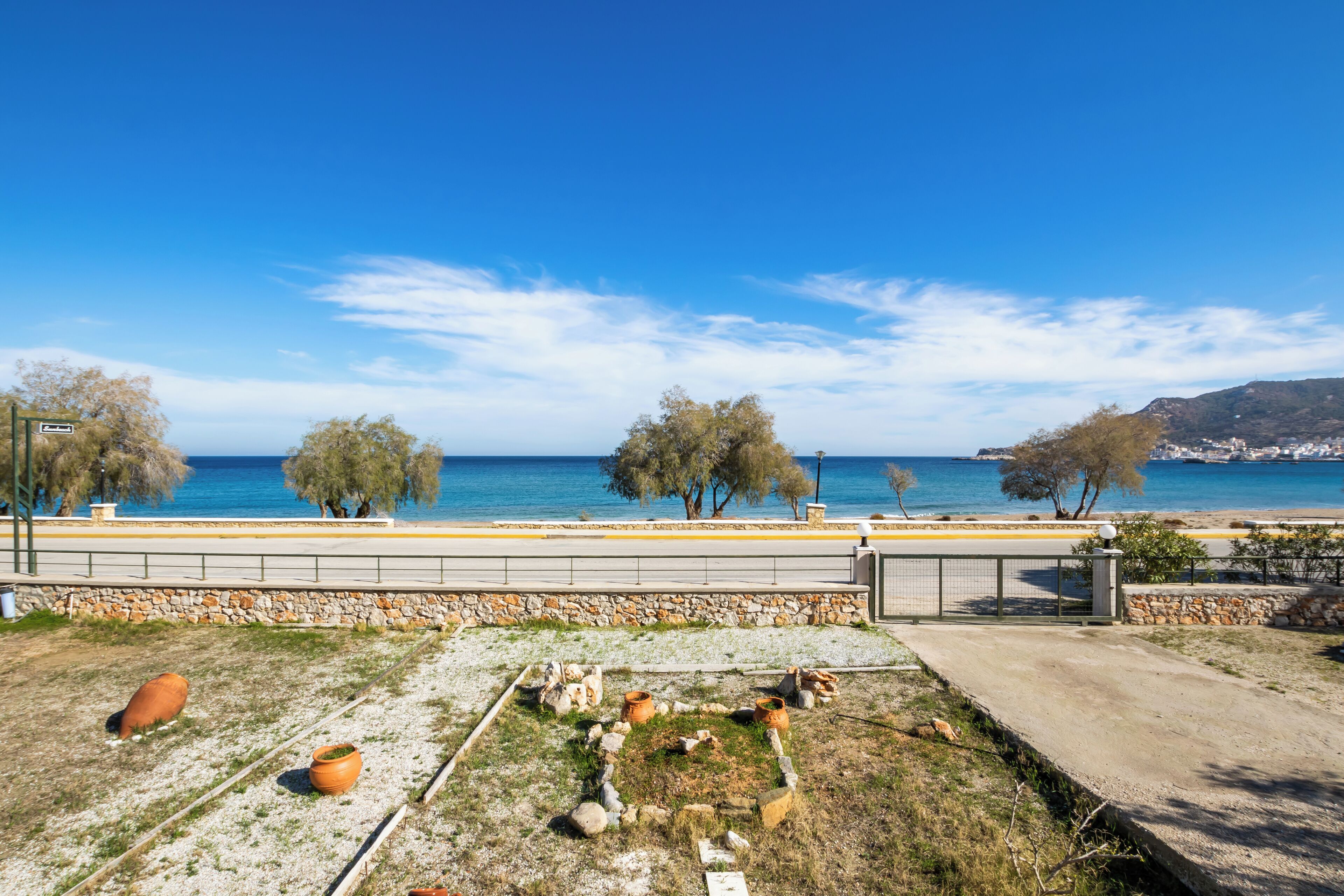 A coastal landscape with a clear sky, a paved walkway, and a view of the sea.