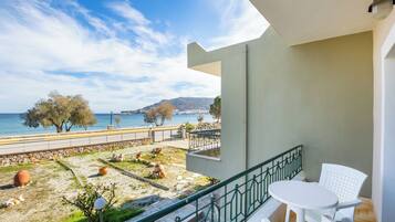 Un balcón con vista al mar, una mesa y silla blancas, y una pequeña zona ajardinada con plantas y un perro.