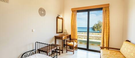 A bedroom with a bed, a desk, a chair, and a large window with a view of the sea.