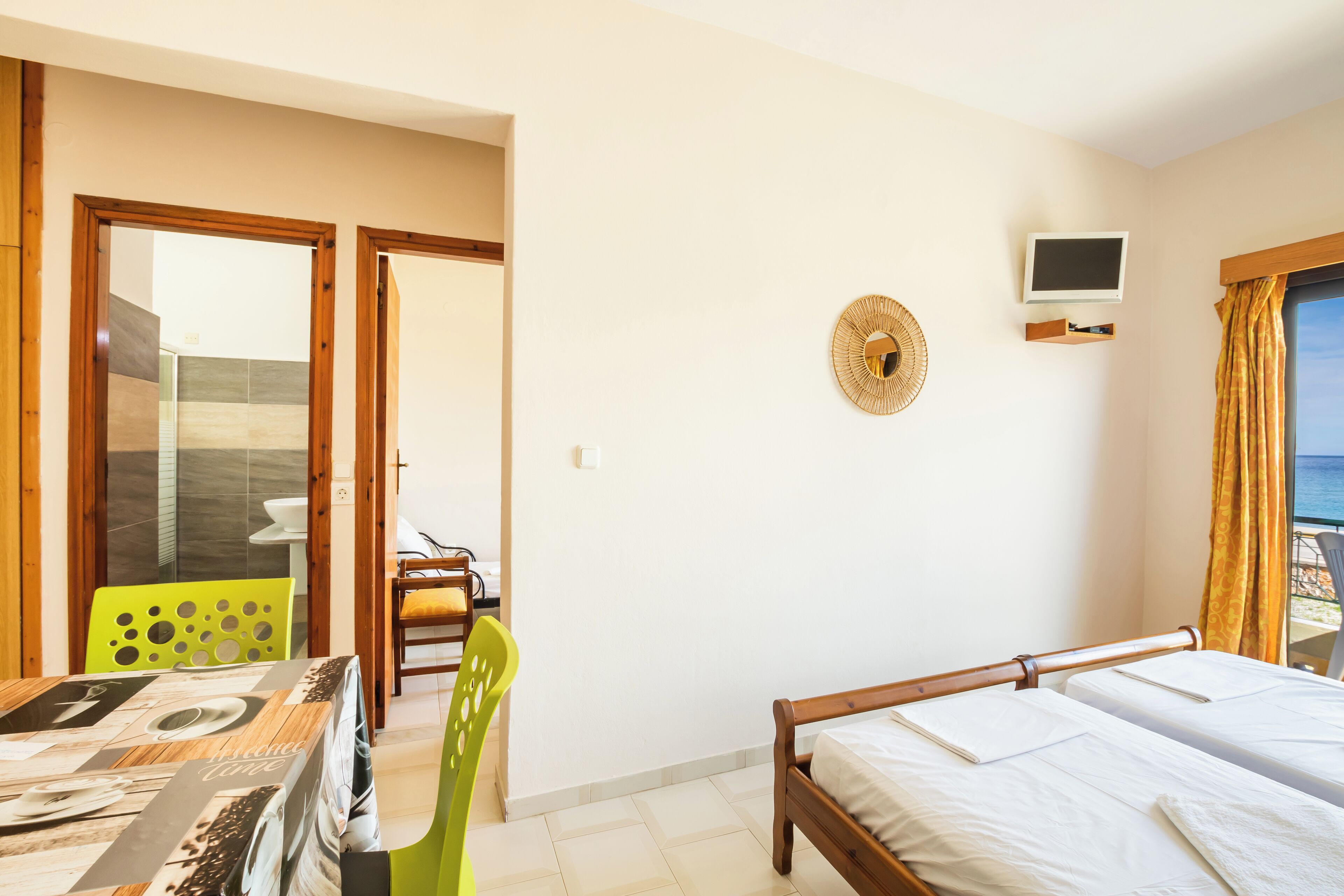 A hotel room with a bed, a dining table, a chair, a TV, and a view of the sea.