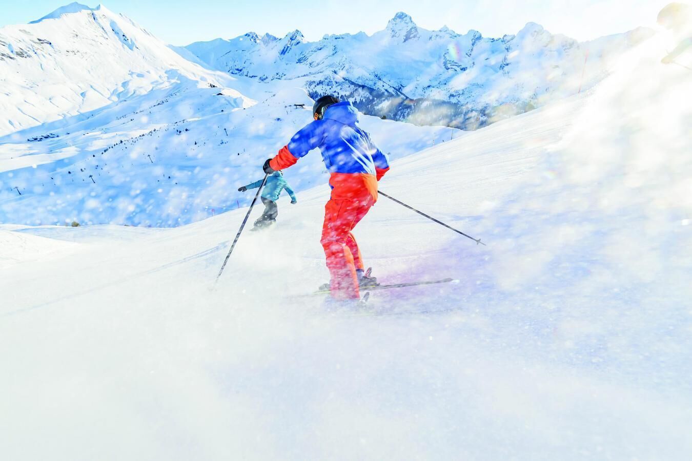 Une personne fait du ski sur une pente enneigée, avec des montagnes en arrière-plan.