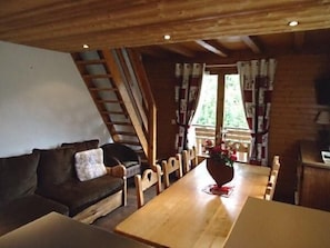 A cozy room with a wooden ceiling, a sofa, a dining table, and a window with curtains.