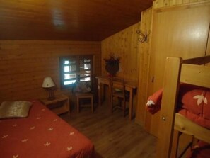 A wooden room with a bed, a desk, and a chair.