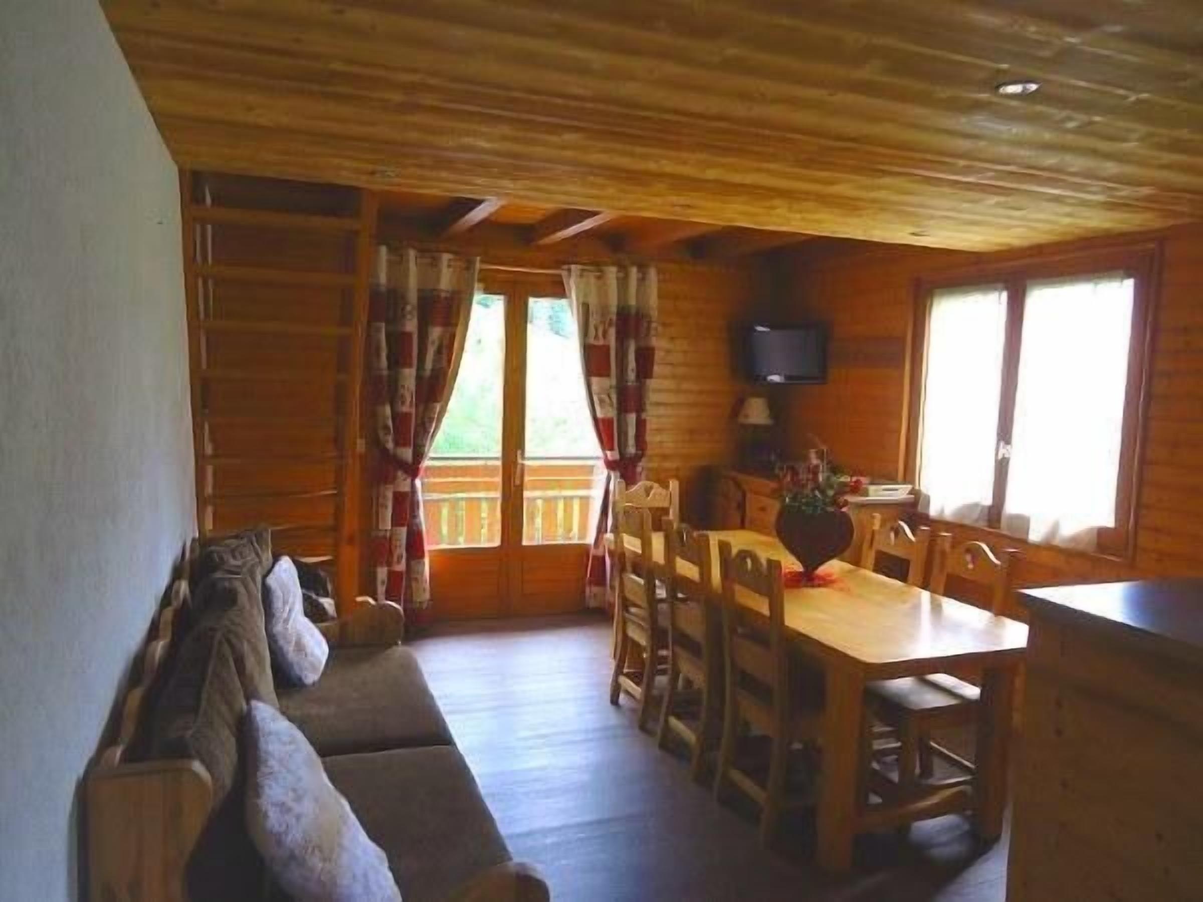 Interior de una cabaña de madera con una mesa de comedor, sillas, un sofá y un televisor.