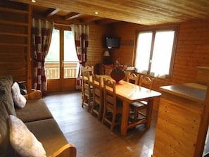 A cozy cabin interior with a wooden dining table, chairs, a sofa, and a TV mounted on the wall.