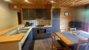Eine kompakte Küche mit dunklen Schränken, einer Holzausziehtafel, einer Spüle, einem Herd und einem Essbereich mit Tisch und Stühlen.
