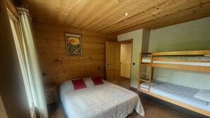 Ein Schlafzimmer in einer Holzhütte mit Etagenbett, einem Einzelbett mit roten Kissen, einer Holztür und einem Gemälde an der Wand.