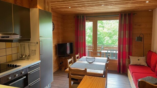 Ein gemütliches Blockhauss-Interieur mit Küche, Essbereich und einem roten Sofa.