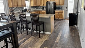 Una cocina moderna con armarios de madera, un refrigerador de acero inoxidable, un microondas y un comedor con un taburete y sillas.