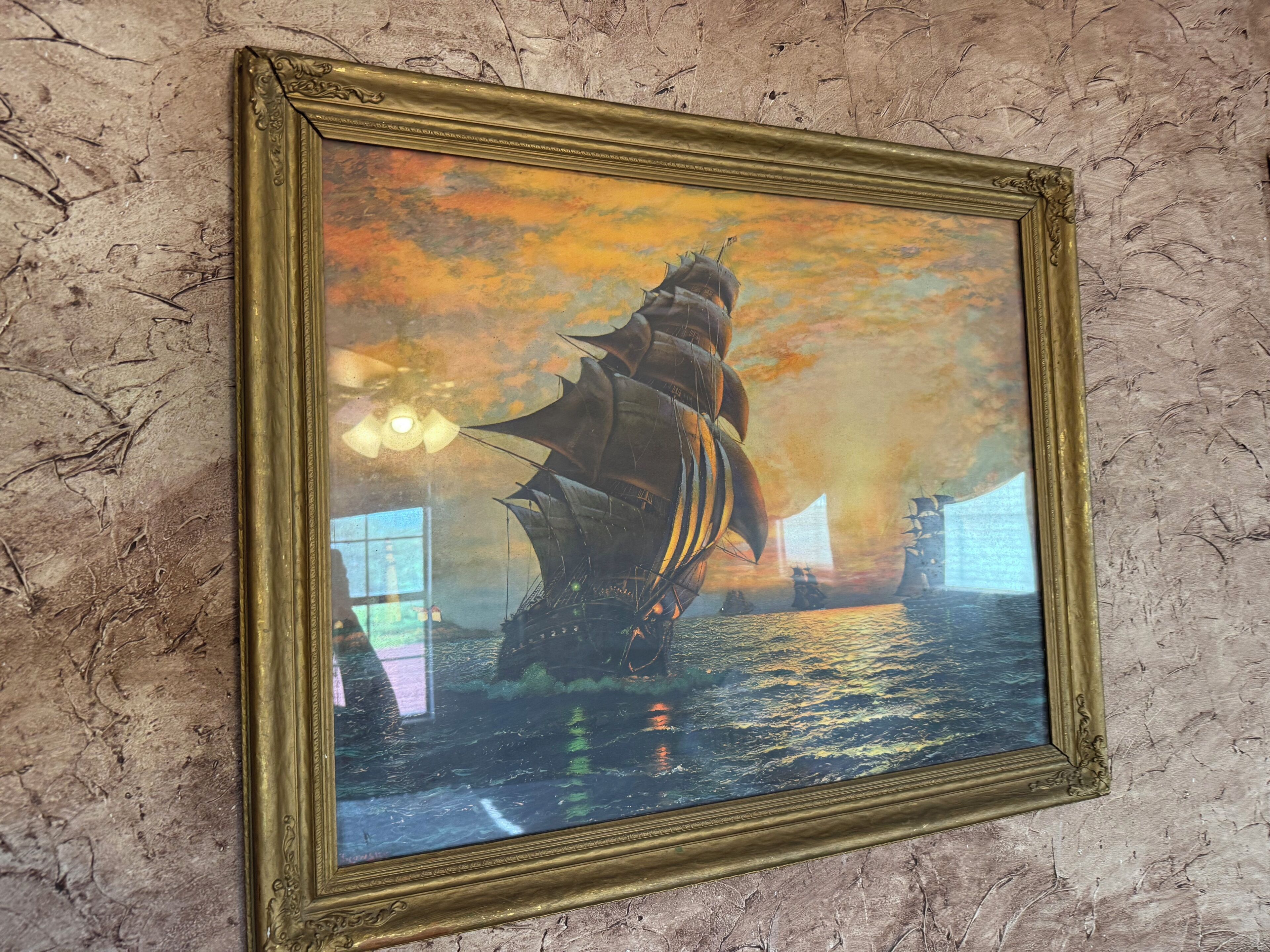 Ein gerahmtes Kunstwerk, das ein Schiff auf dem Wasser bei untergehender Sonne zeigt.