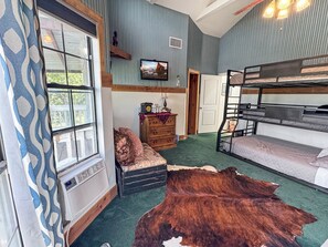 Ein Zimmer mit Etagenbett, einem gemusterten Vorhang, einer Holzkommode, einem Fernseher und einem großen Teppich.