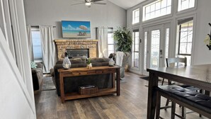 Una sala de estar amplia con chimenea, un televisor montado encima y una zona de comedor con una mesa y un banco de madera.