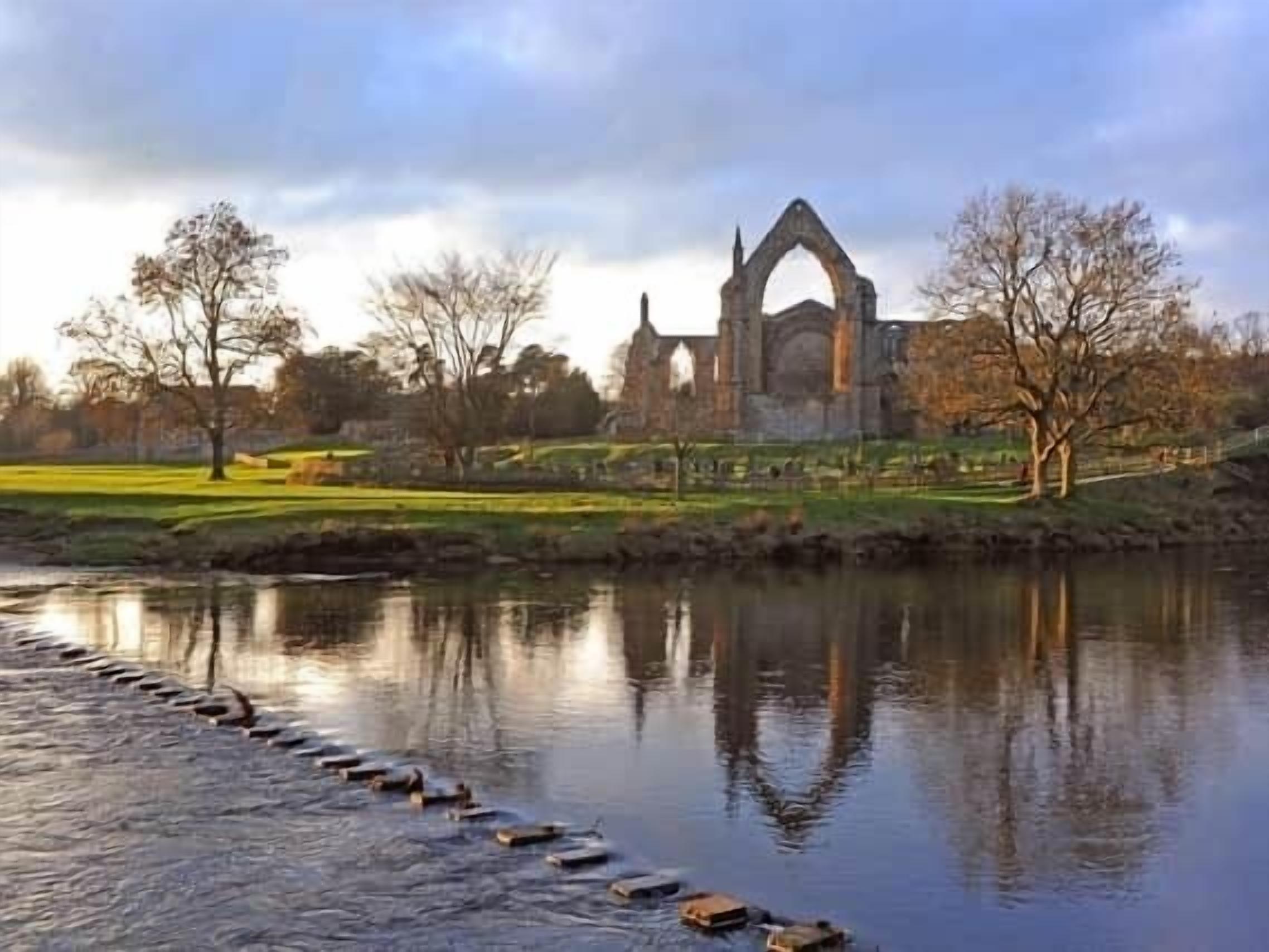 A historic building with a prominent arch structure, surrounded by a calm river and a park with trees.
