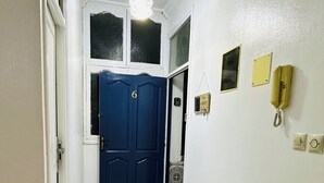 A hallway with a blue door, a patterned rug, a chandelier, and wall-mounted light switches. - Large apartment with Rooftop in a private, secure, family-friendly building! (Al Aaroui)