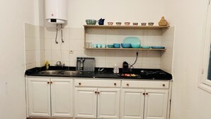 A kitchen with white cabinets, a black countertop, a sink, and a range hood. There are shelves above the countertop holding bowls and a pitcher. - Large apartment with Rooftop in a private, secure, family-friendly building! (Al Aaroui)