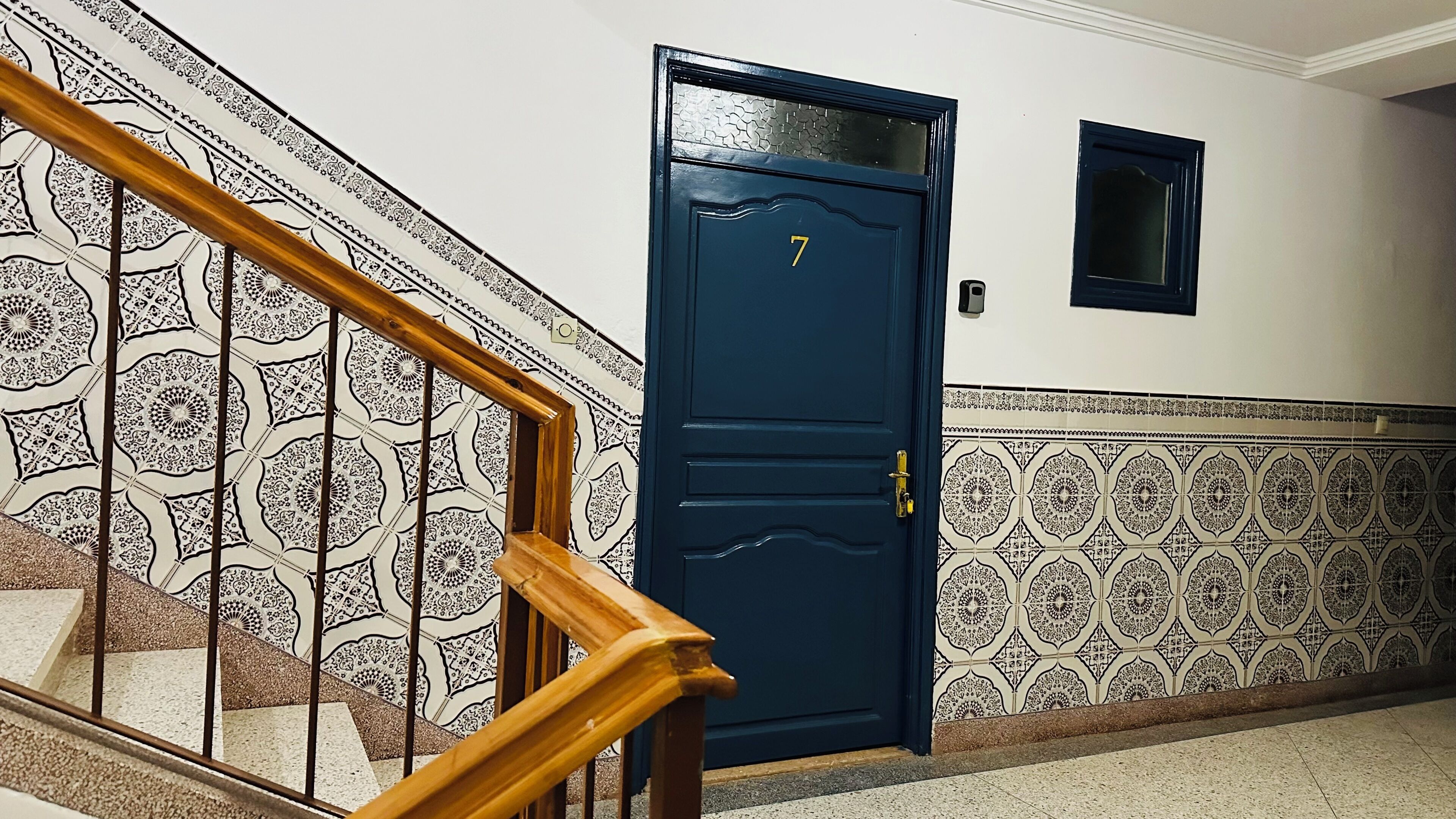 Un escalier avec une rampe en bois menant à une porte bleu foncé portant le numéro 7.