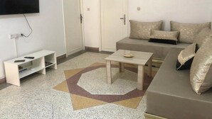 A living room with a sofa, a coffee table, a TV mounted on the wall, and a door. - Large apartment with Rooftop in a private, secure, family-friendly building! (Al Aaroui)