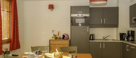 A compact kitchen with a dining area, featuring a wooden table, chairs, a microwave, a sink, and a red hanging light.