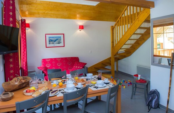 A dining area with a wooden table set for breakfast, a red patterned sofa, and a staircase.