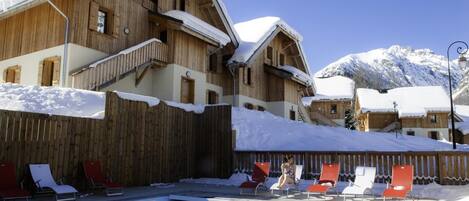A wooden building with a pool area, surrounded by snow-covered mountains.
